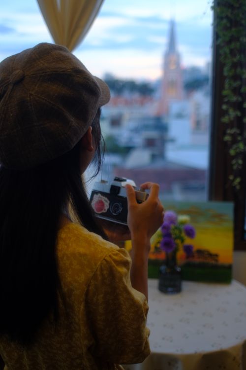 Free A woman holding a vintage camera captures a stunning sunset view through a window. Stock Photo