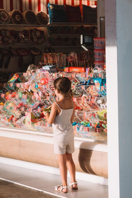 Free Young girl in summer clothes looking at colorful candy display in a shop. Stock Photo