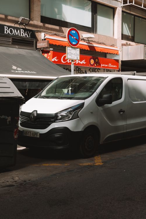 Free White Renault van parked on a busy city street with urban building backdrop. Stock Photo