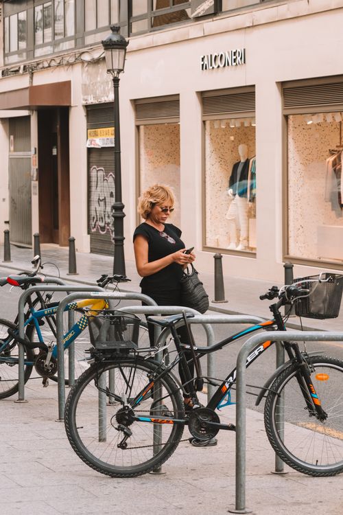 Free Blonde woman using smartphone by parked bicycles outside a modern shop in a city street. Stock Photo