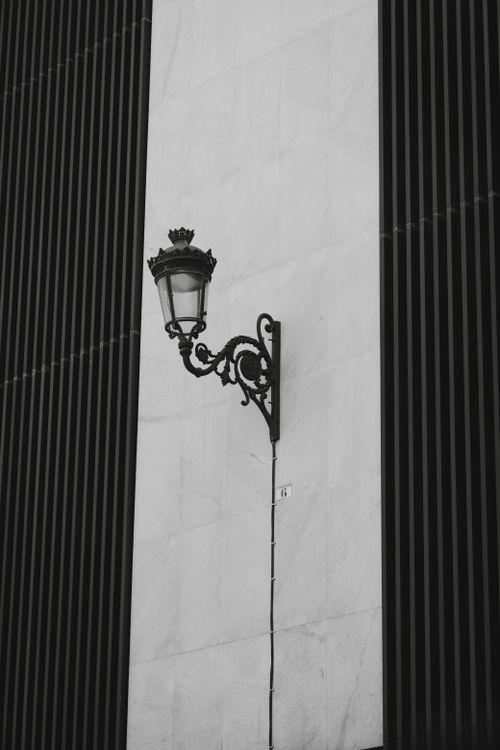 Free Black and white image of a vintage street lamp mounted on a modern building façade. Stock Photo