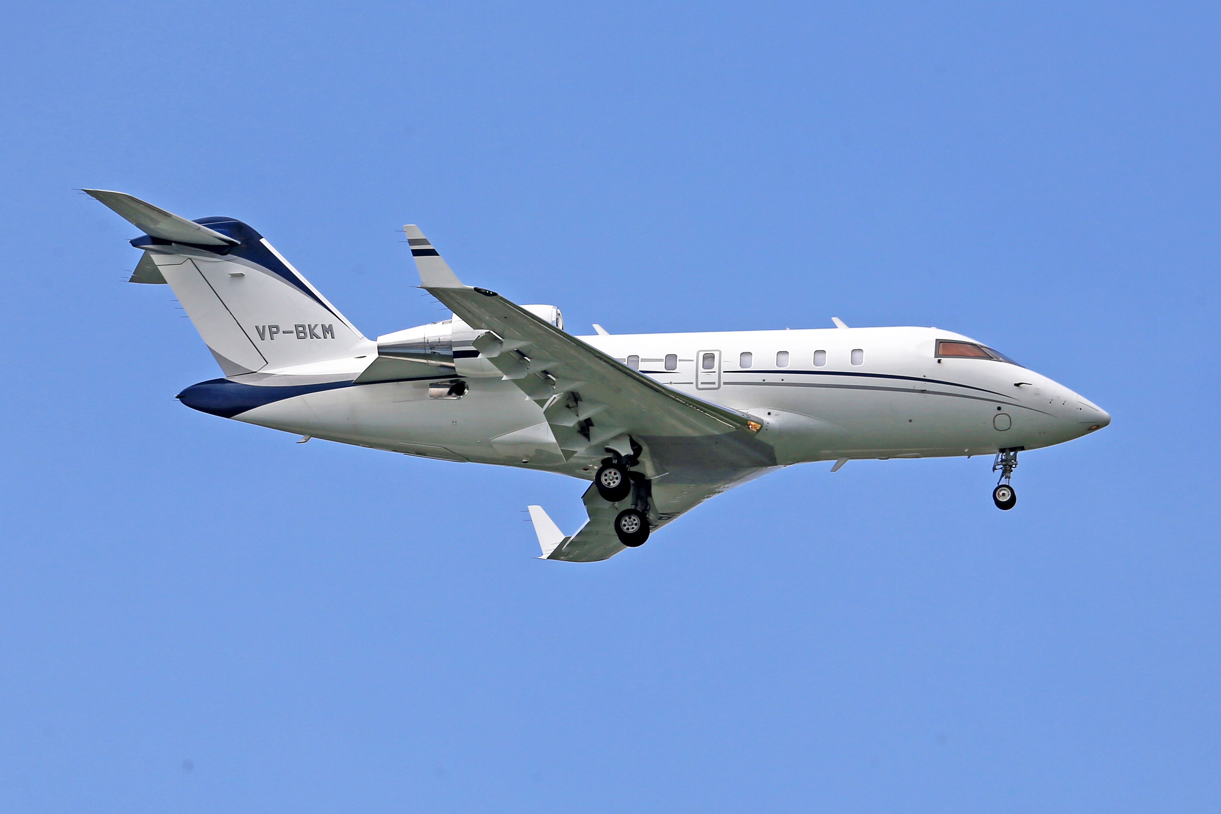 White private jet in flight against a clear blue sky, showcasing luxury air travel.