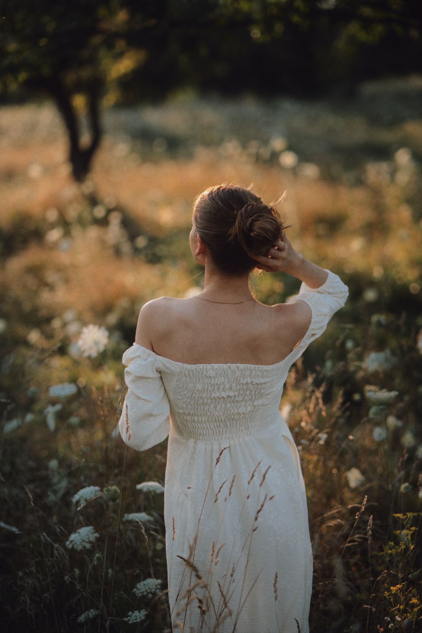 A woman in a white off-the-shoulder dress in a meadow at sunrise