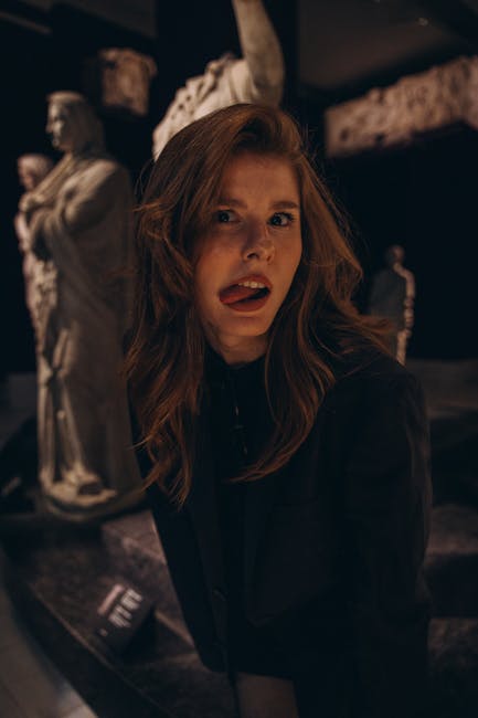Woman making an expression in a dim museum with classical sculptures.