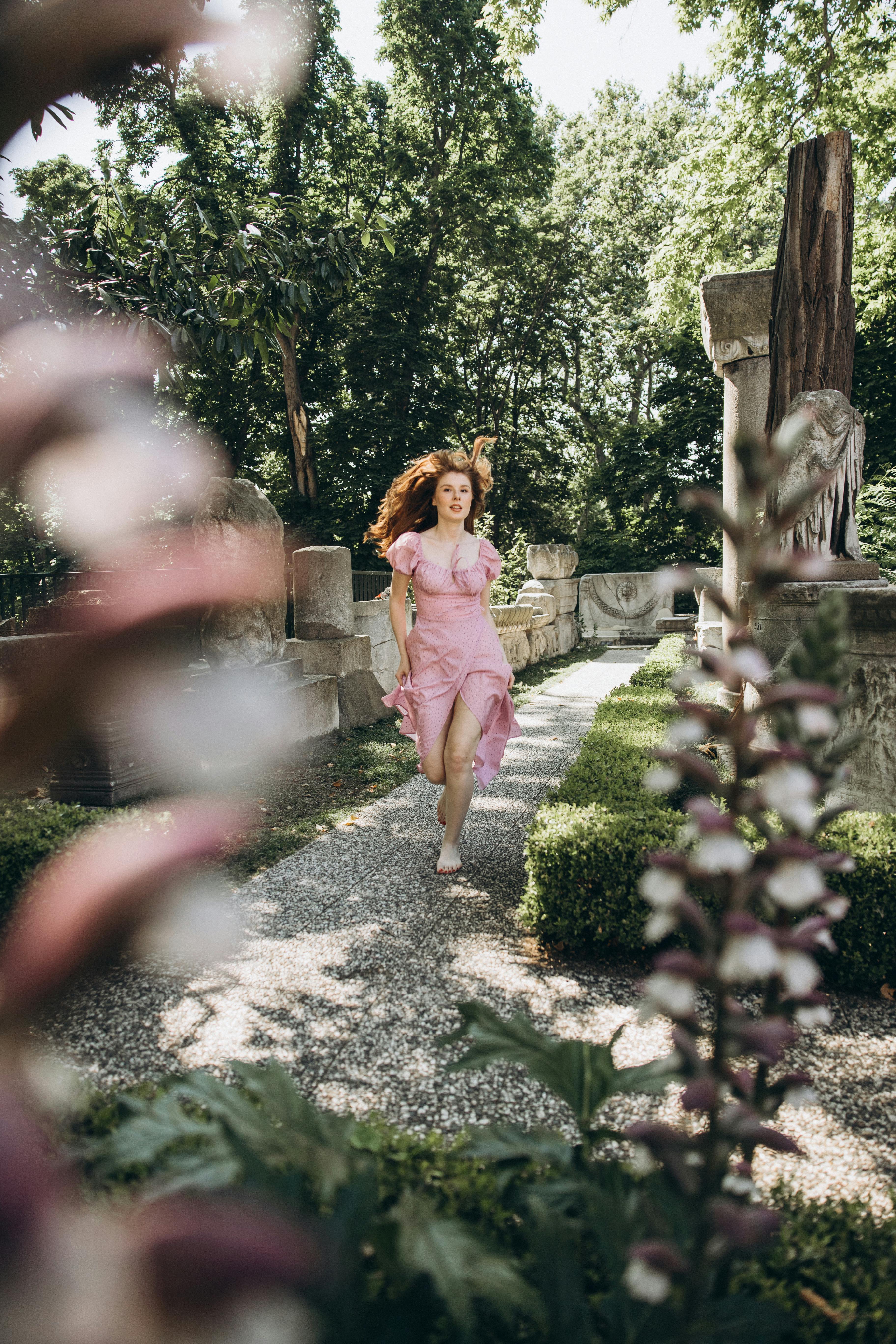 a woman in a pink dress running through a garden