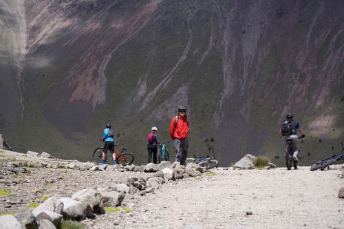 Free Group of cyclists mountain biking on a rugged hilltop trail amidst dramatic landscapes. Stock Photo