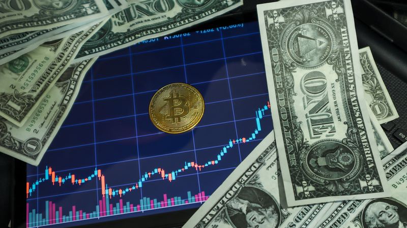 Bitcoin coin on a tablet showing stock chart, surrounded by dollar bills.
