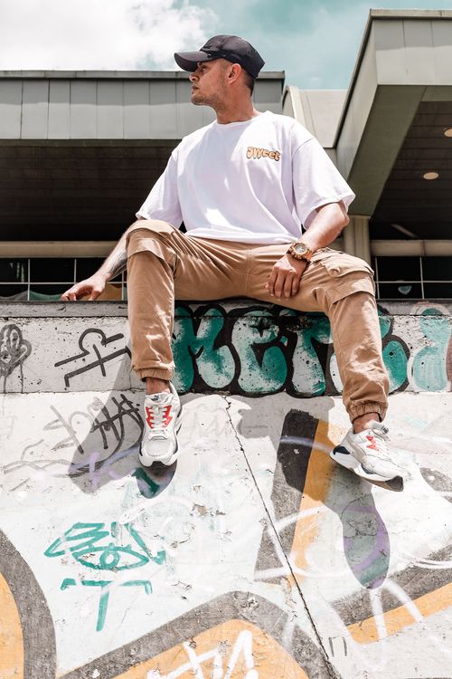 Free A young man in casual attire relaxes at a graffiti-covered skate park, enjoying a sunny day. Stock Photo