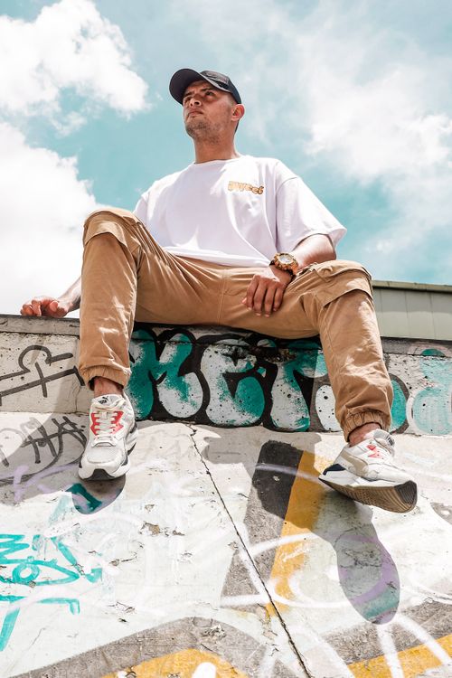Free Low angle shot of a stylish man sitting on a graffiti-covered wall under a bright sky. Stock Photo
