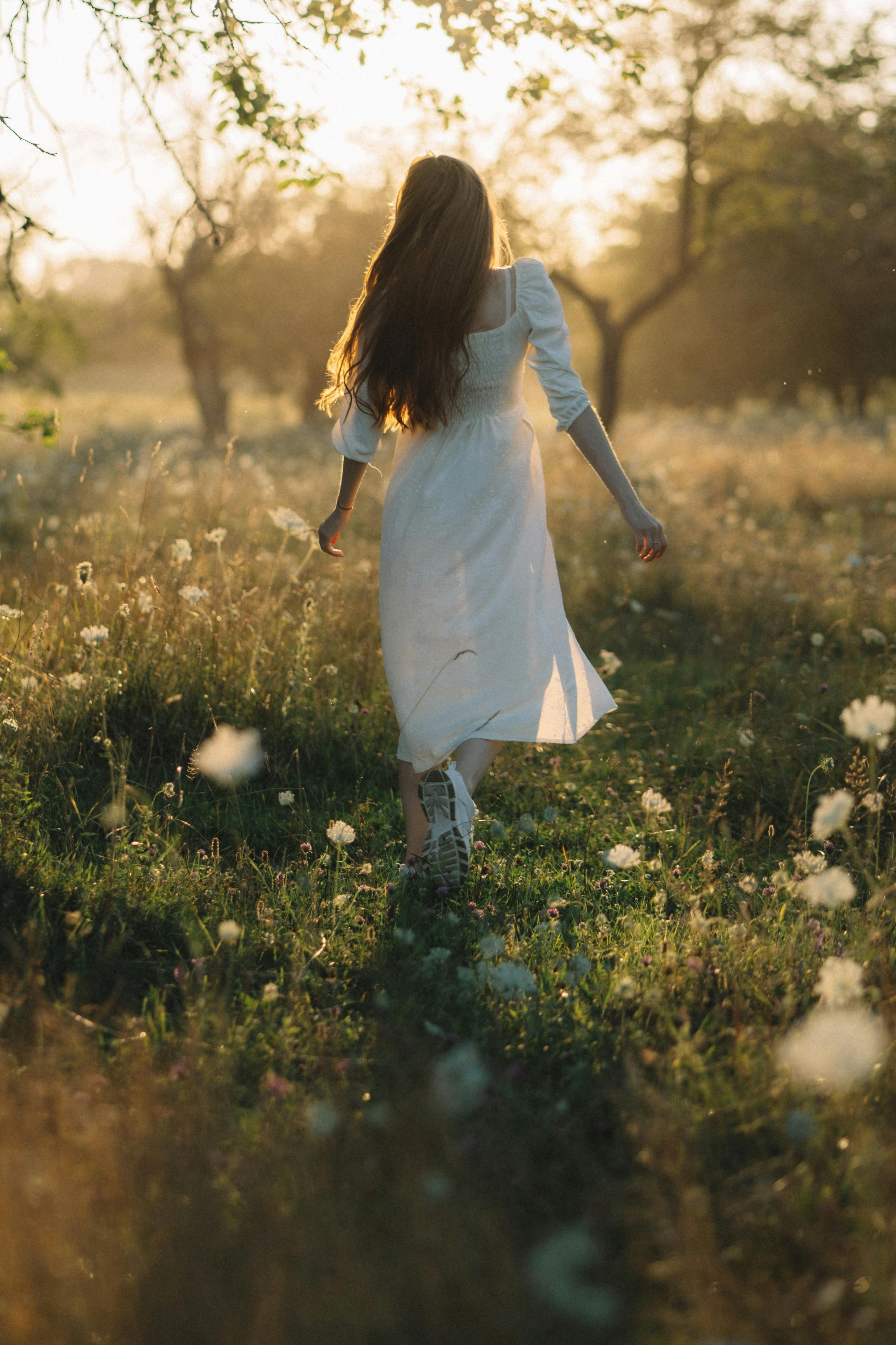 A serene scene of a young woman in a white dress walking through a sunlit meadow in summer.