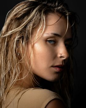 Close-up portrait of a blonde woman with wet hair and piercing in a moody setting.