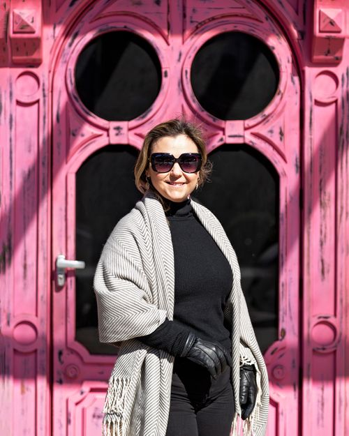 Free A woman in a fashionable outfit stands confidently in front of a vibrant pink door, showcasing style and elegance. Stock Photo
