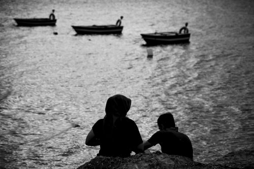 Free A serene black and white silhouette of people by the sea with distant boats. Stock Photo