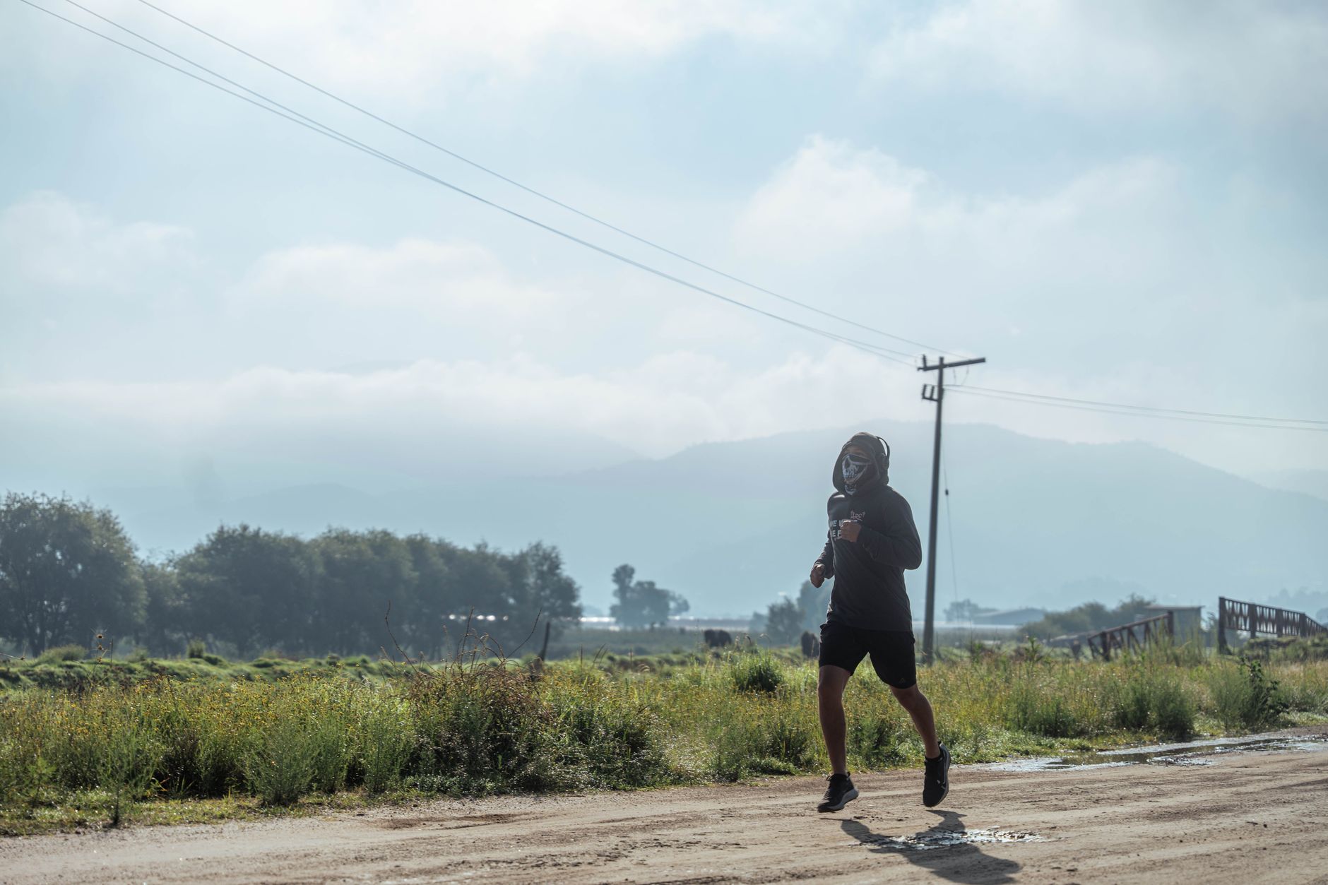 A person jogging on a rural dirt road with mountains in the background, creating a serene outdoor exercise scene.