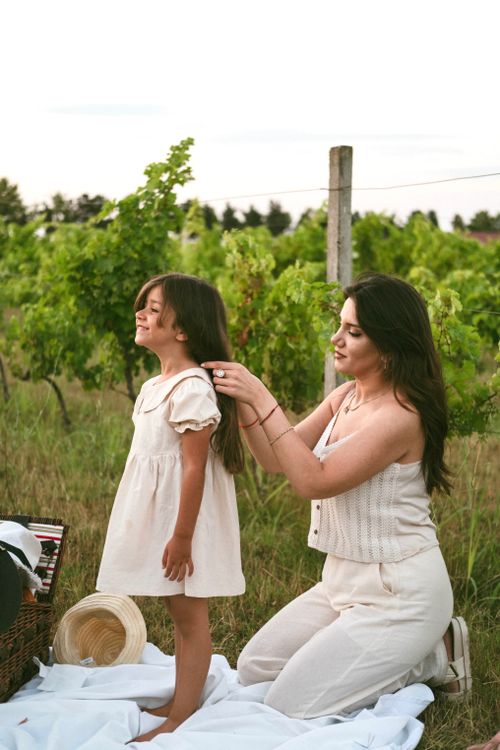 Free A woman braids a child's hair in a serene vineyard setting, symbolizing love and connection. Stock Photo