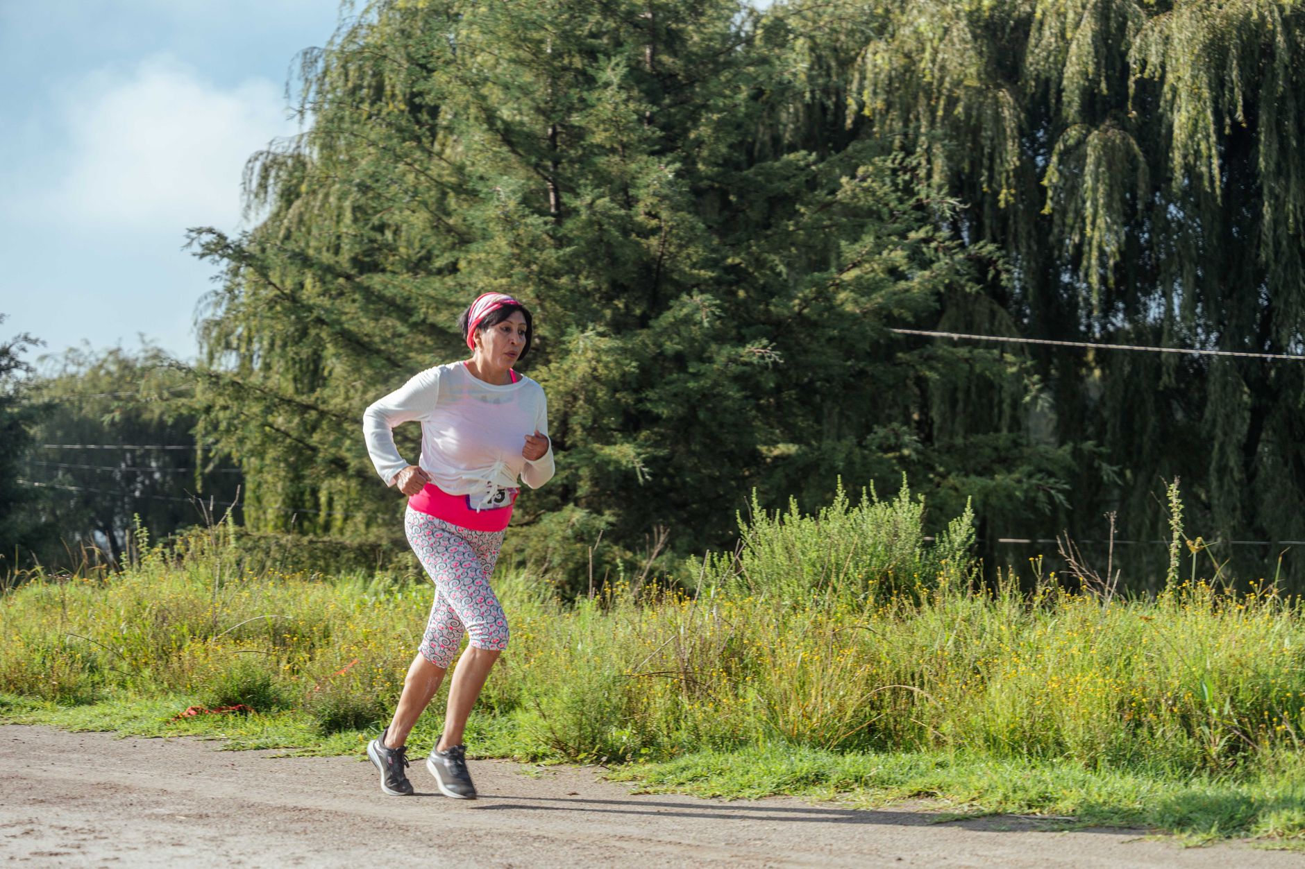 Woman jogging along a forest path under the bright sun, embracing nature and fitness.