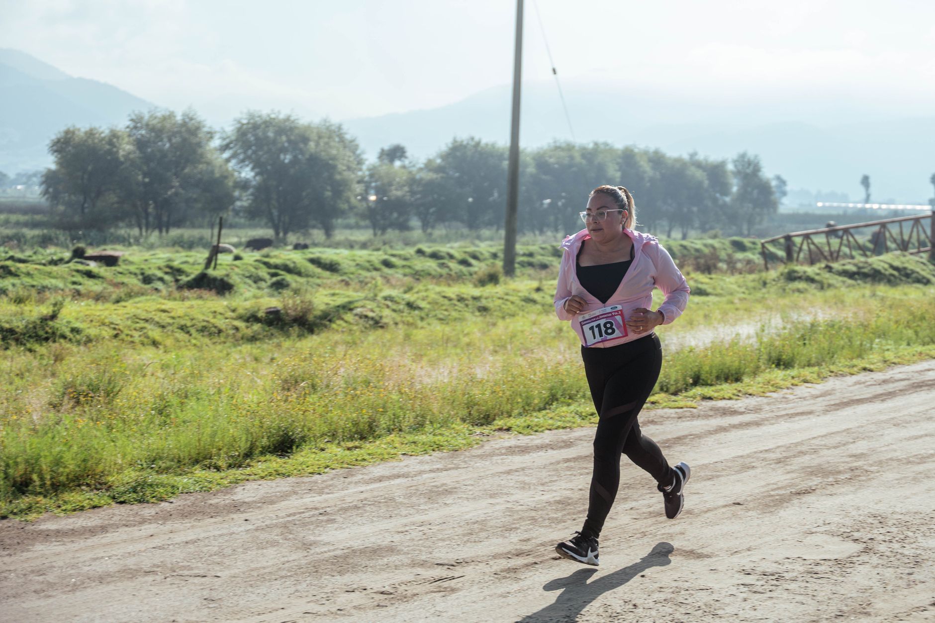 Woman jogging on a rural road during daylight, surrounded by lush greenery and mountains.