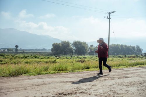 Free A woman jogs on a sunny day along a rural countryside dirt road. Stock Photo