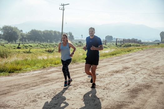 Active couple jogging on a dirt road in a scenic rural area under the bright sun.