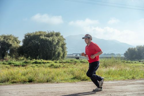 Free A middle-aged man jogging on a rural dirt road, surrounded by greenery and mountains. Stock Photo
