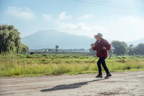 Free Senior woman jogging on a rural path with mountains in the background on a sunny day. Stock Photo
