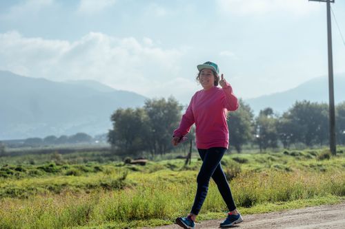 Free A cheerful woman enjoys a walk on a rural dirt road with green fields and mountains in the background. Stock Photo