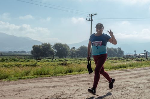 Free A joyful runner flashes a peace sign on a sunny day in a rural setting with mountains in the background. Stock Photo