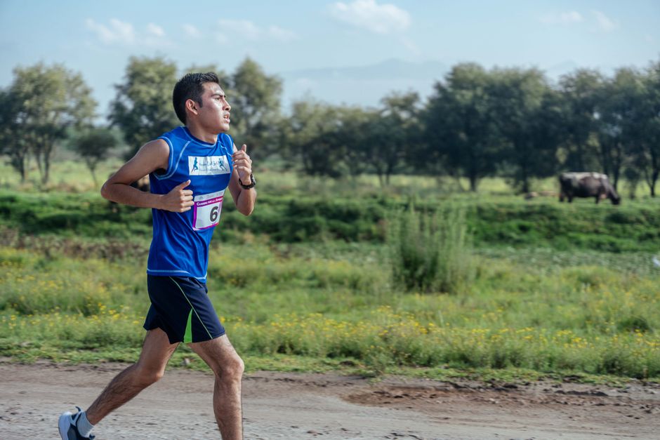 Man jogging on a rural road surrounded by nature, wearing sportswear and racing bib.
