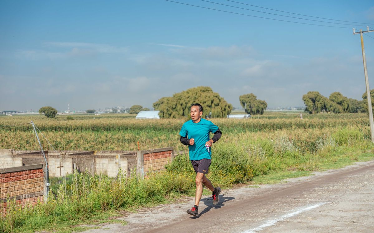 Man jogging on a country dirt road surrounded by fields under a clear blue sky.