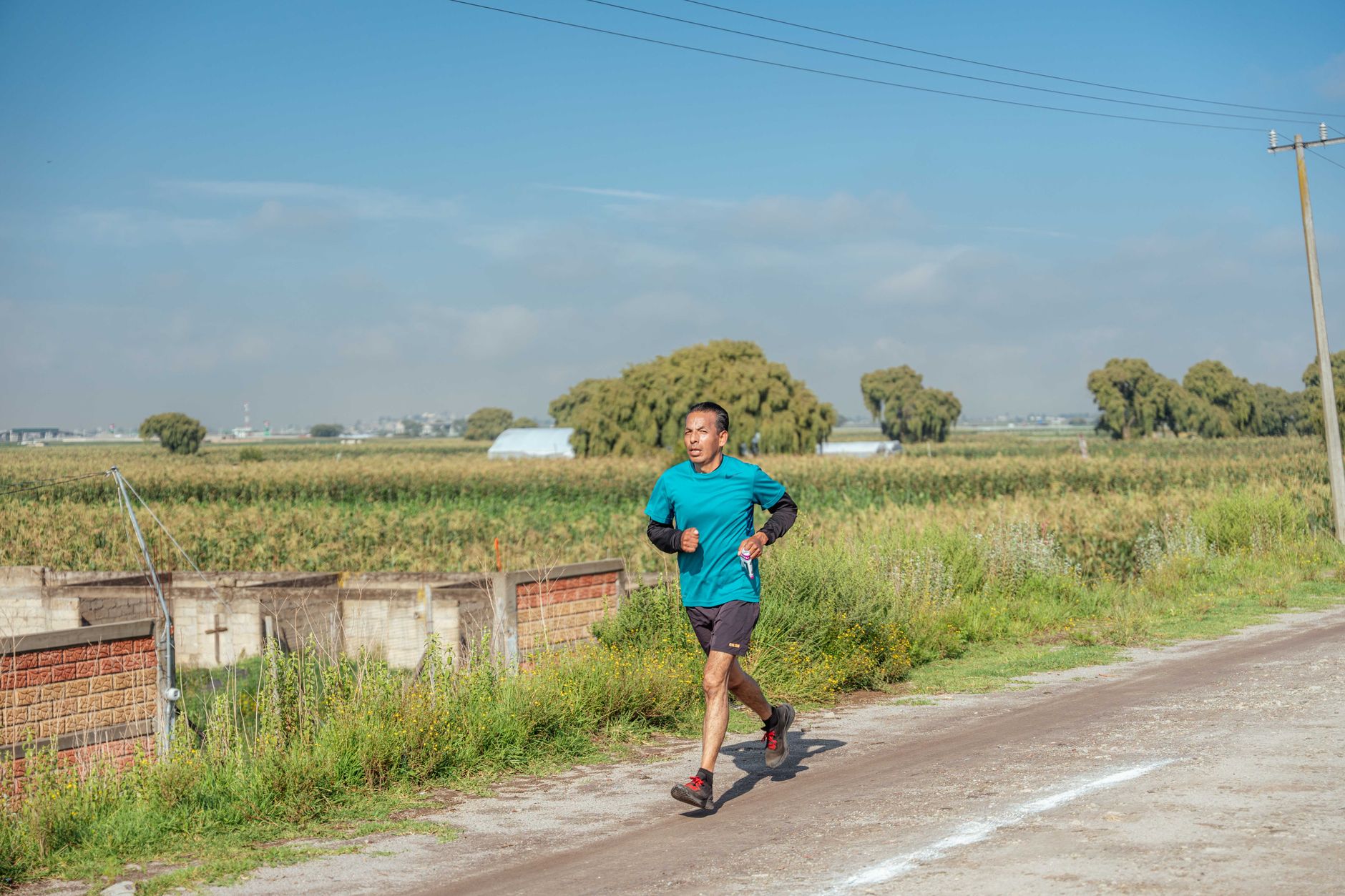 Man jogging on a country dirt road surrounded by fields under a clear blue sky.