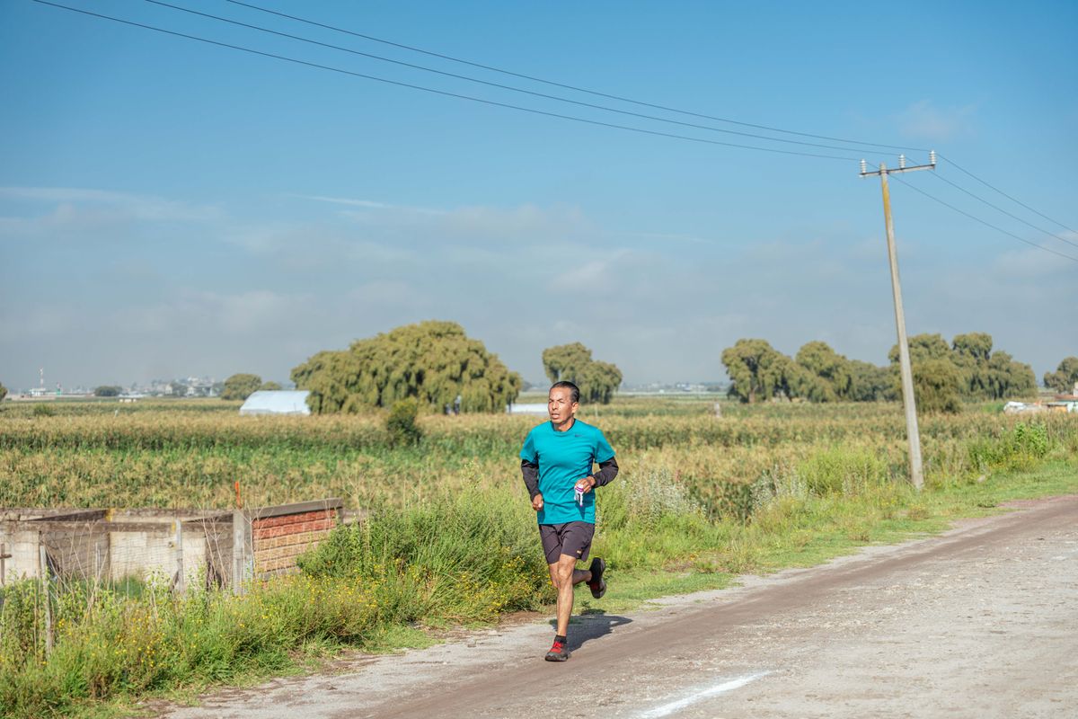 A man jogging at a relaxed easy pace along a quiet rural road between green fields on a sunny day