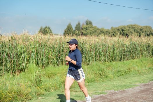 Woman jogging along a rural path next to a cornfield, enjoying fitness in nature.