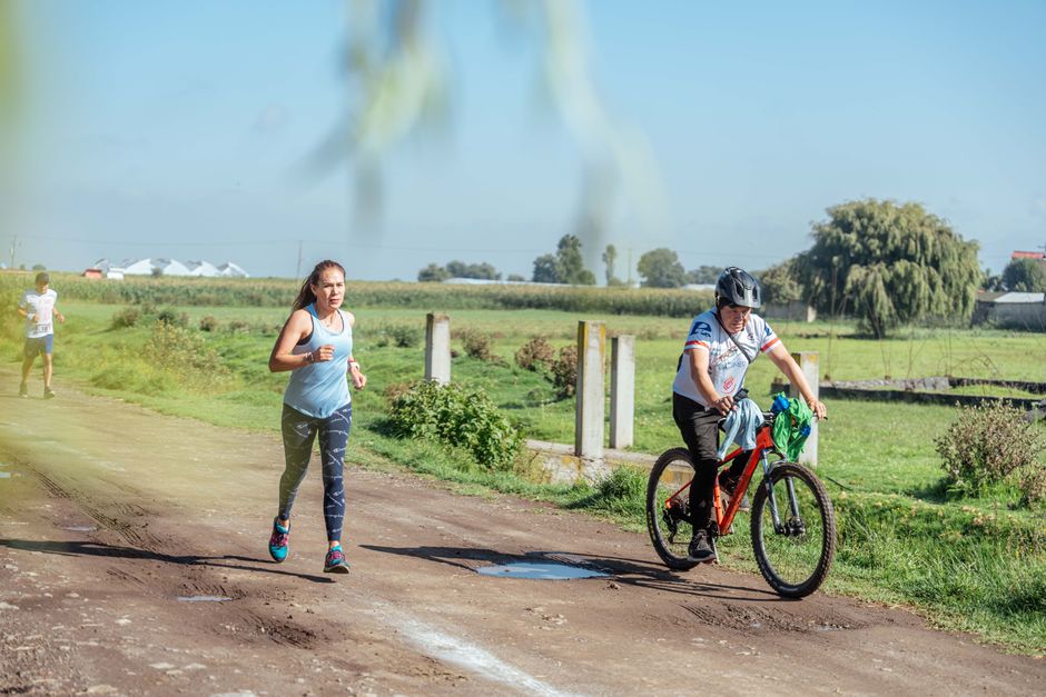 Woman running and man cycling on a sunny rural path surrounded by greenery.