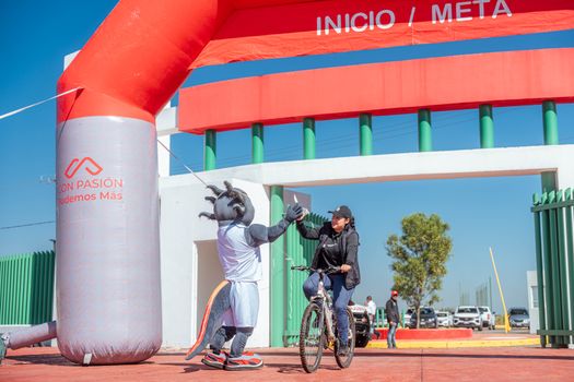 A cyclist receives a high-five from a mascot at the finish line of a cycling event under a clear blue sky.