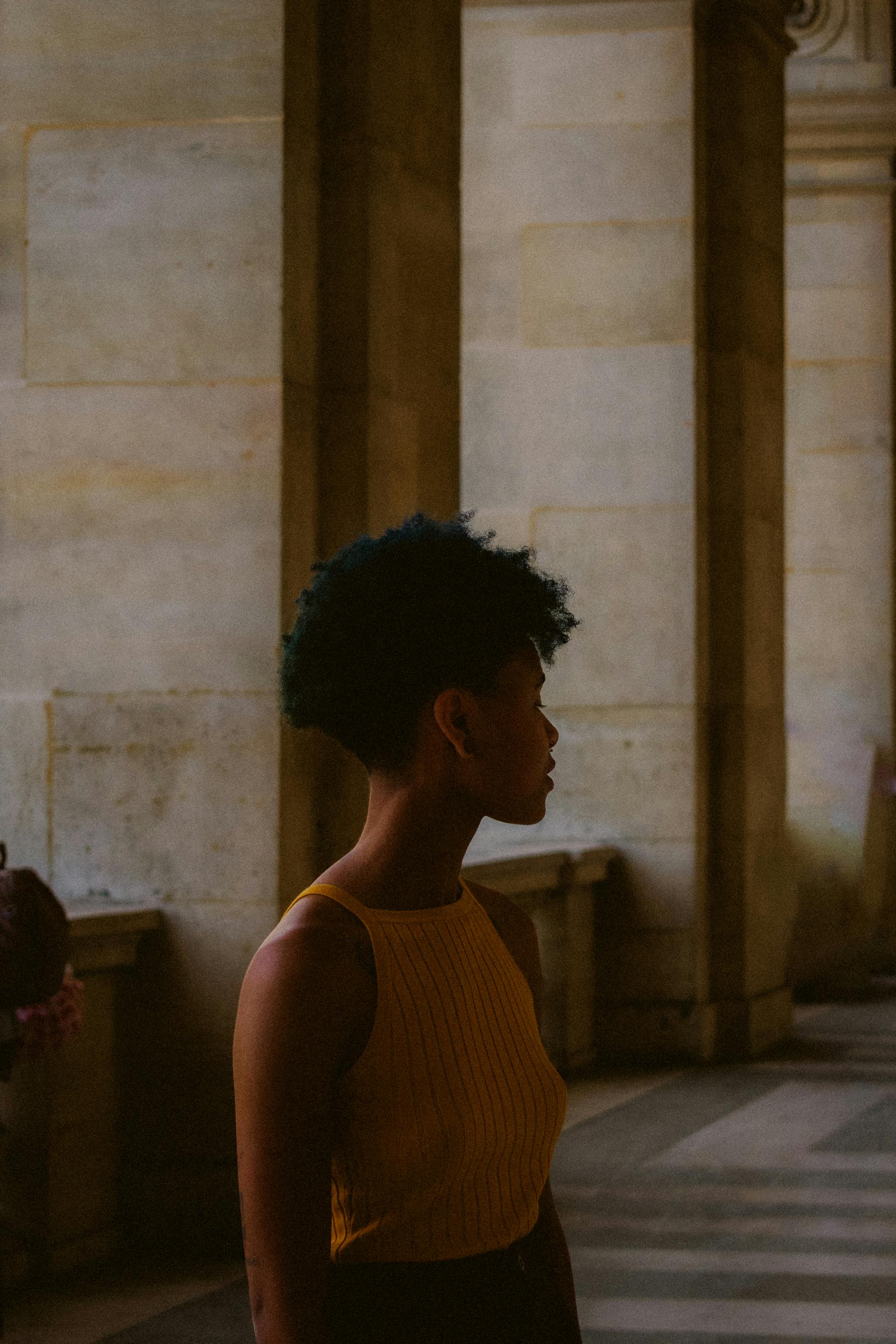 A woman in a yellow top poses in a dimly lit historical building with stone columns.