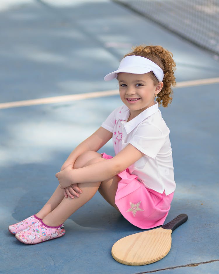 Smiling Girl With Tennis Racket Sitting On Court