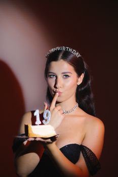 A young woman celebrates her 19th birthday with a cake in a studio setting, wearing a Happy Birthday crown.
