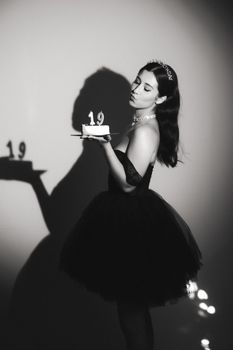 Young woman in a black dress celebrates birthday with cake and crown.