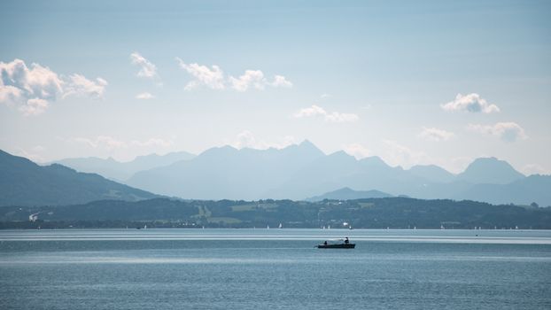 A tranquil scene of a fishing boat on a vast lake with distant mountains.