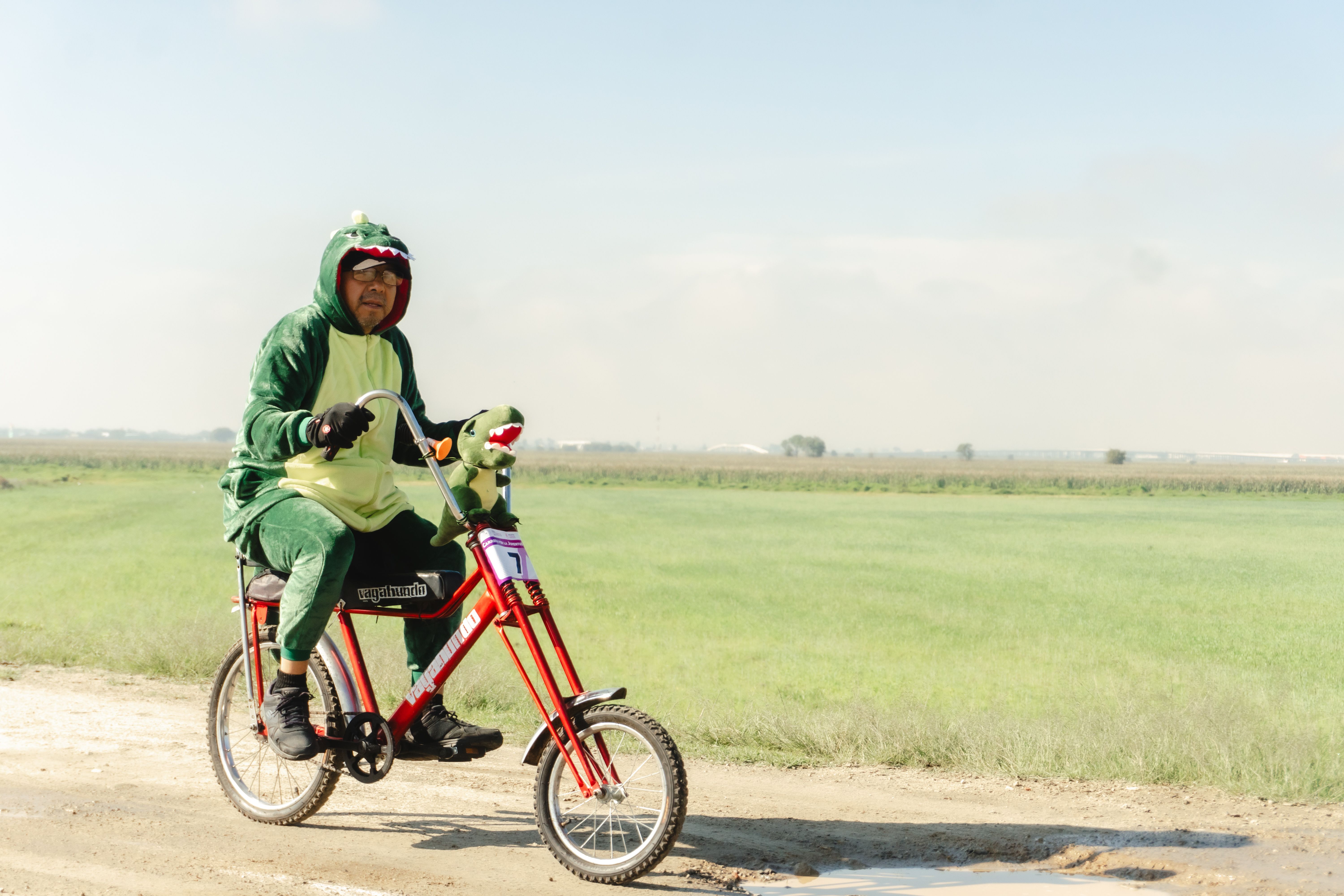 A man dressed as a dinosaur rides a bicycle through the fields of Santa María Atarasquillo, Mexico.