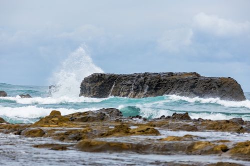 Free Vivid waves crash against rugged rocks under a cloudy sky, capturing coastal nature's raw power. Stock Photo