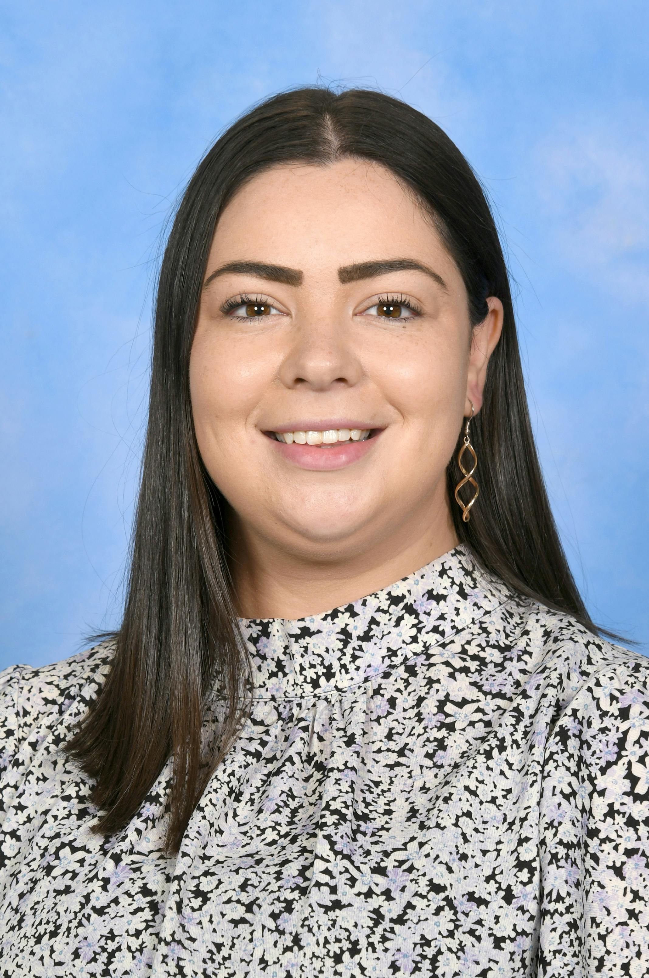 Portrait of a smiling woman with black hair and a floral blouse against a blue background.