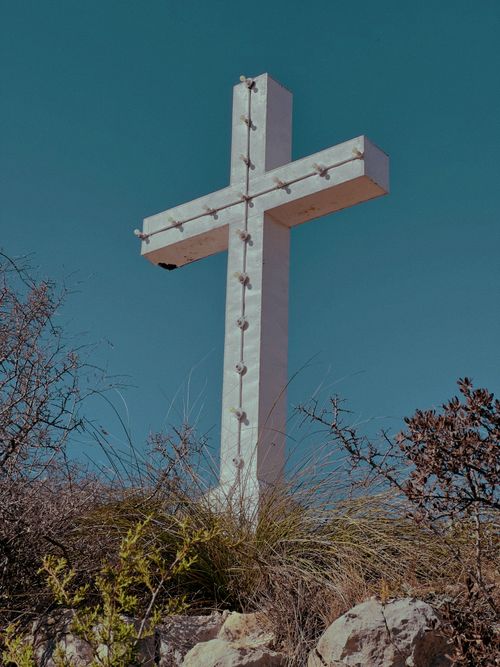 Free A large white cross stands prominently on a hill amidst sparse vegetation under a blue sky. Stock Photo