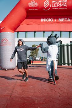 Runner high-fives mascot at the finish line under the arch. Athletic celebration.
