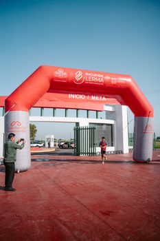 A runner crosses the finish line under a red inflatable arch at an outdoor sports event.