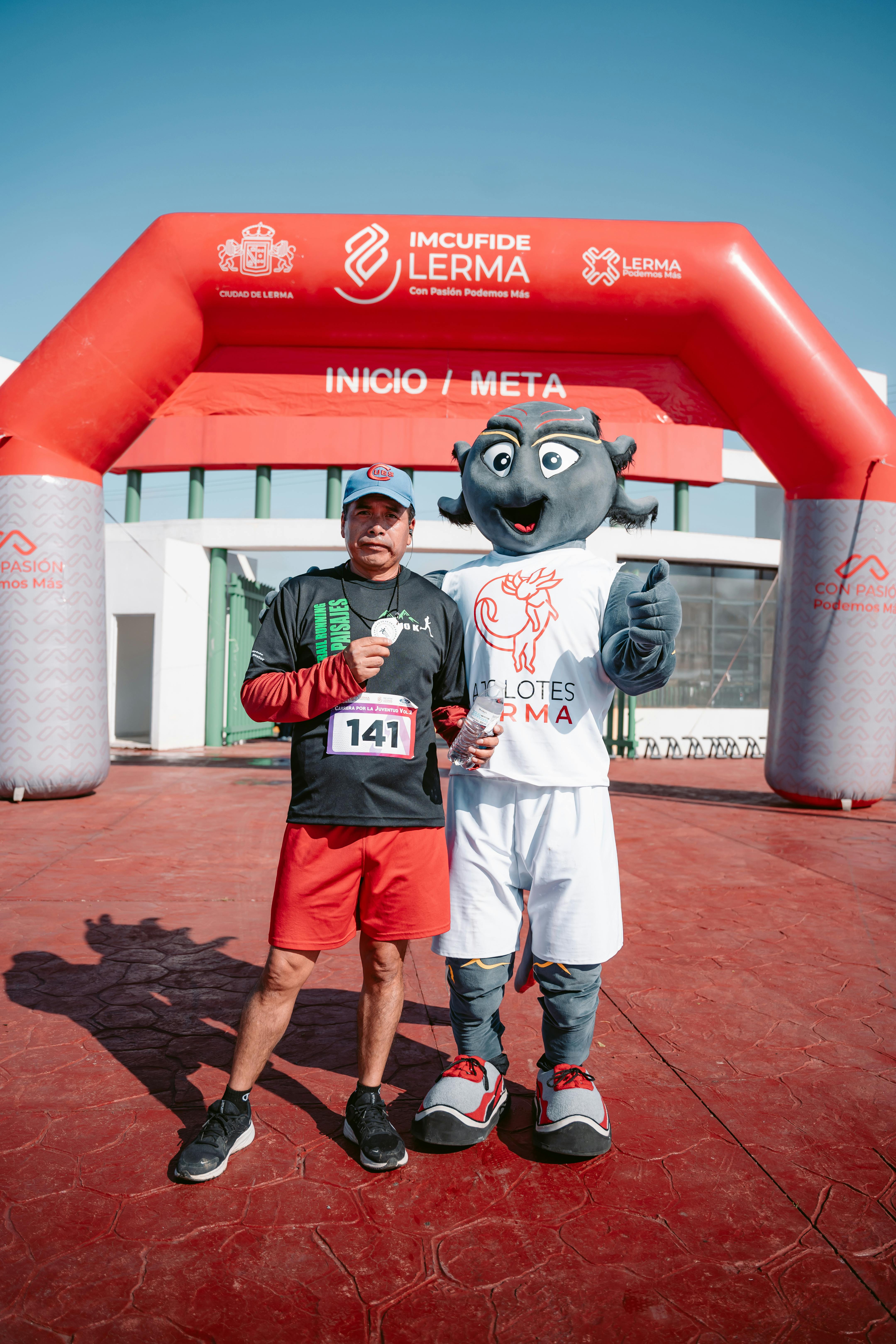 Runner poses with a mascot at the race finish line, portraying joy and achievement.