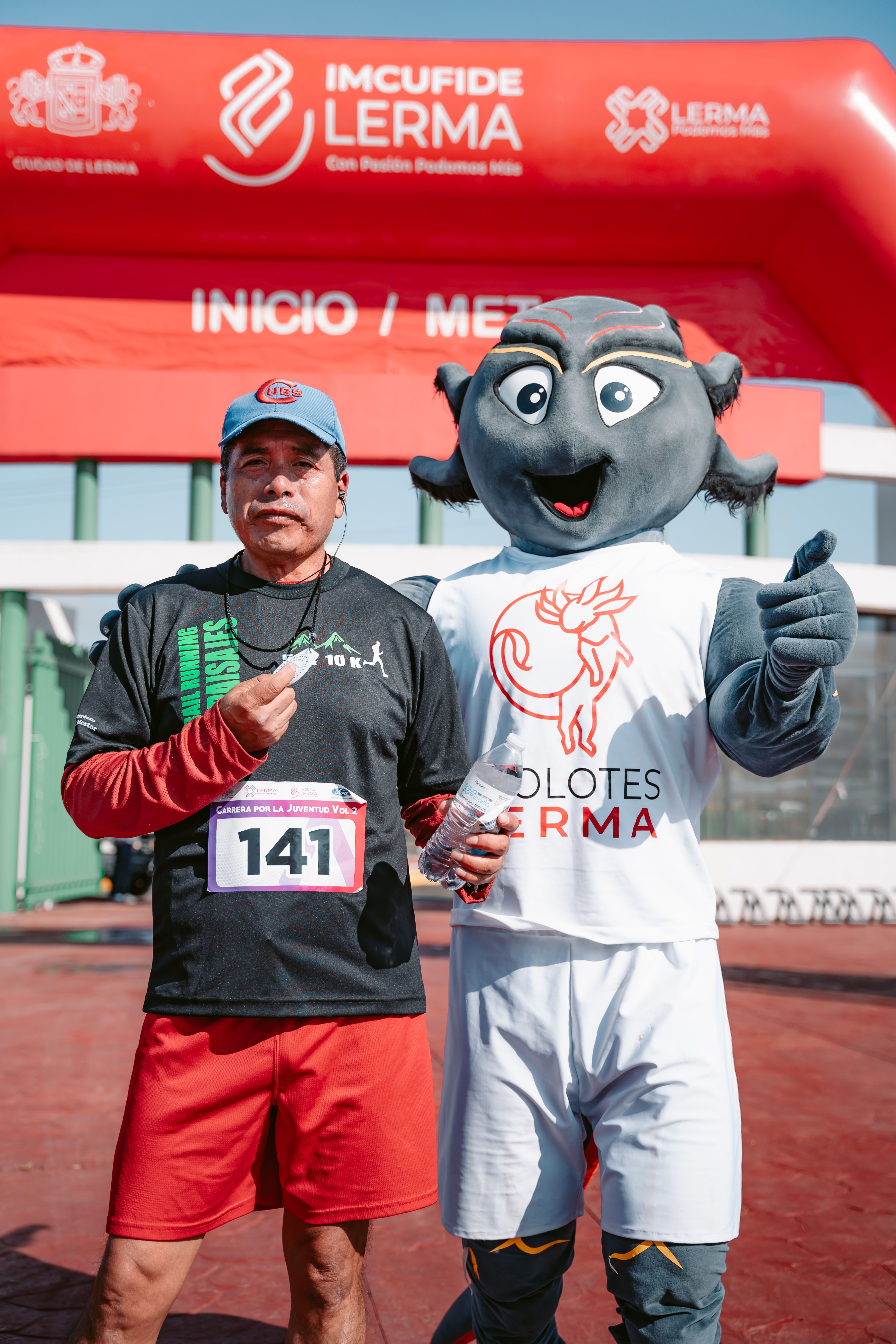Athlete posing with mascot at marathon finish line in Lerma