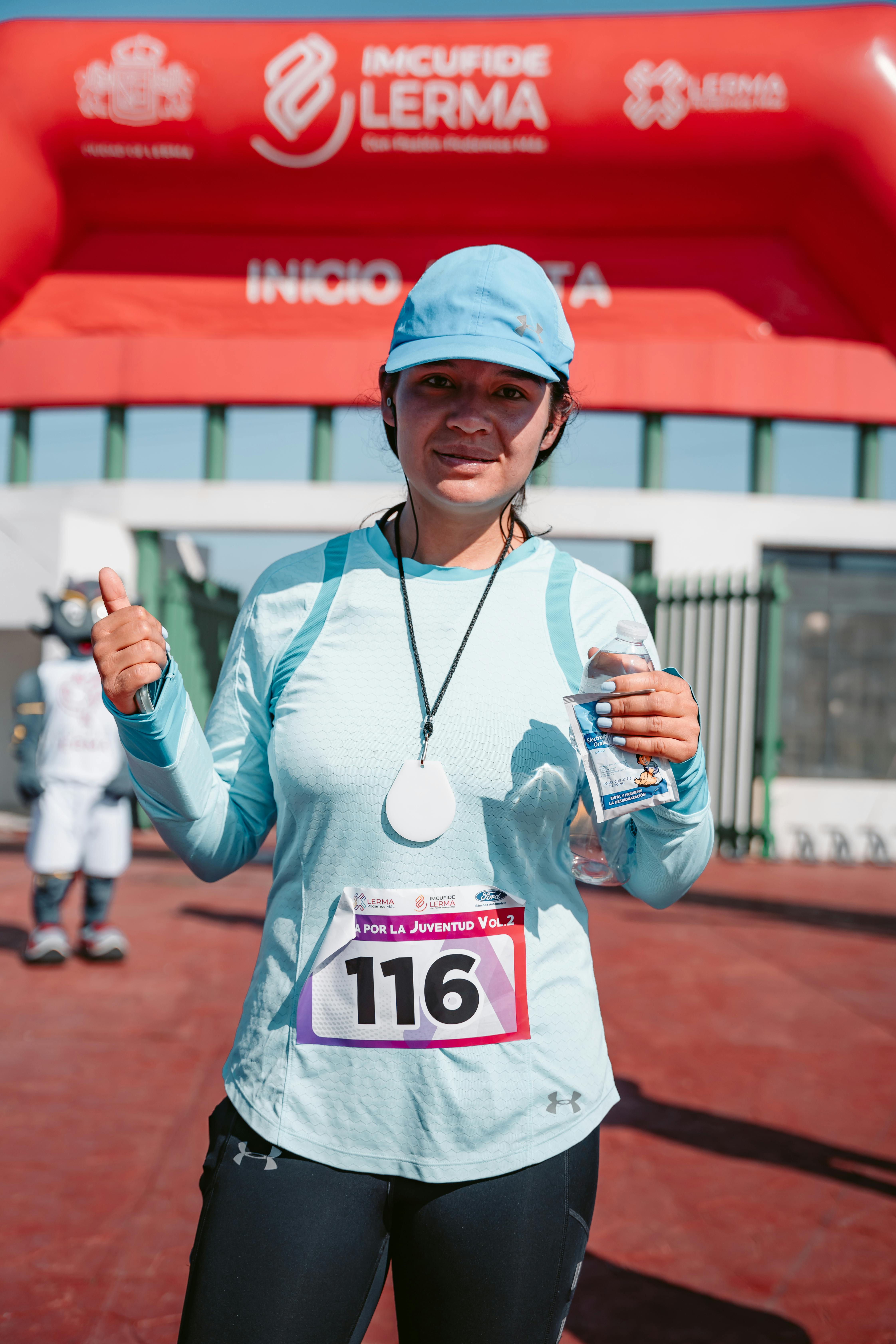 Female runner celebrates completing a race, showing thumbs up at the finish line outdoors.