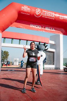 Female athlete at a race finish line in Lerma, posing with a mascot.