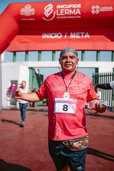 An adult male runner finishes a marathon with joy under a red start/finish arch.